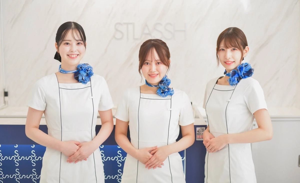 白い制服と青いスカーフを着た3人の日本人女性が笑顔で並んでいます