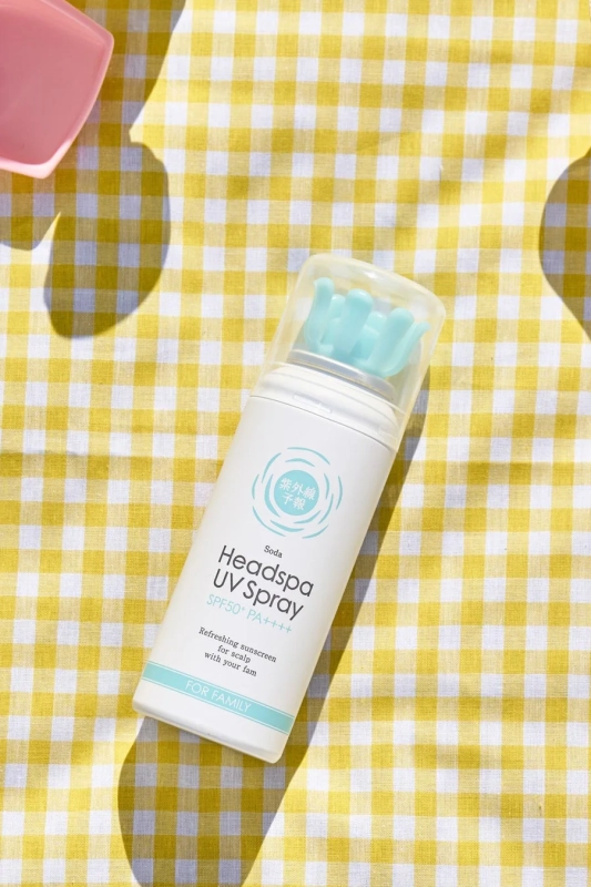 黄色と白のギンガムチェックの布の上に、水色のユニークなキャップが付いた白いヘッドスパUVスプレーが置かれています。