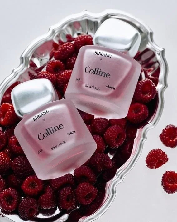 シルバーのトレイに山盛りの新鮮なラズベリーとともに、BIBIANG「Colline」のフロスト加工されたピンク色のヘアセラムボトル