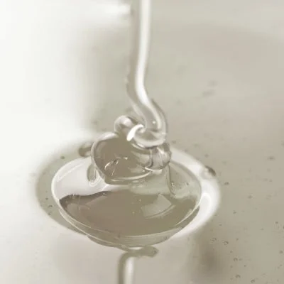 透明でとろみのある液体が、同じ液体の上にゆっくりと注がれている様子をクローズアップで捉えた画像です。光を反射して輝き、その粘性が伝わってきます。