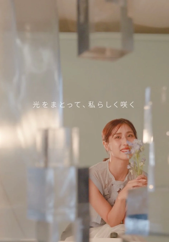 光を浴びて優しく微笑む女性が、小さな花束を手にしています。透明感のある背景と相まって、穏やかで美しい雰囲気が漂う一枚です。