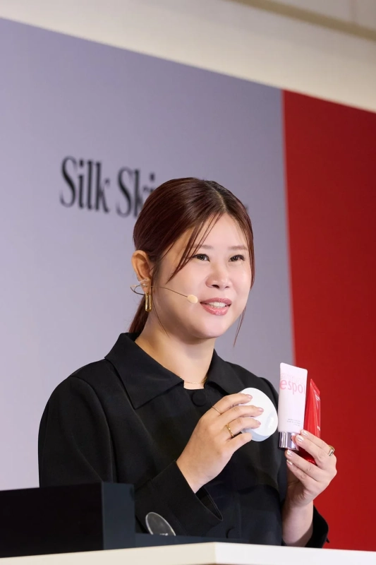 黒い服を着た女性がマイクを装着し、化粧品を手にプレゼンテーション