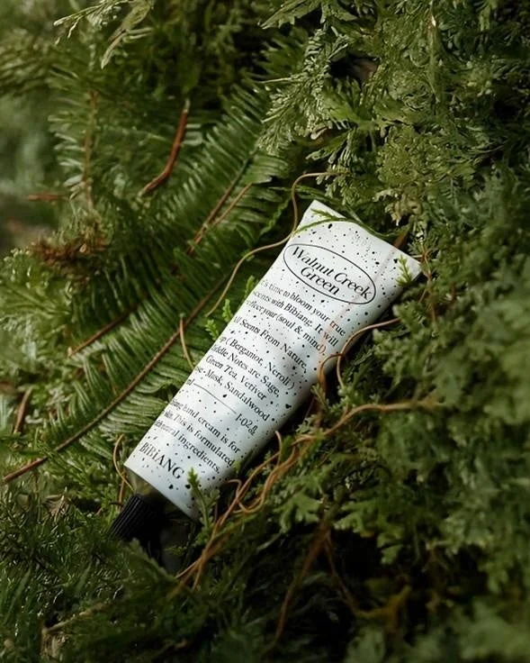 緑豊かな植物の中に置かれた、"Walnut Creek Green"という名前のBIBIANG製ハンドクリームのチューブ
