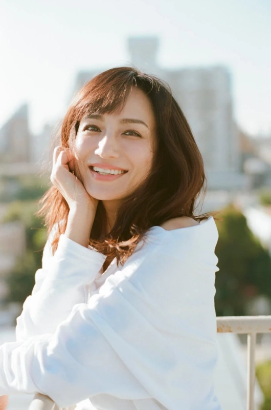 白いシャツを着た女性が屋上のような場所で楽しそうに微笑んでいます