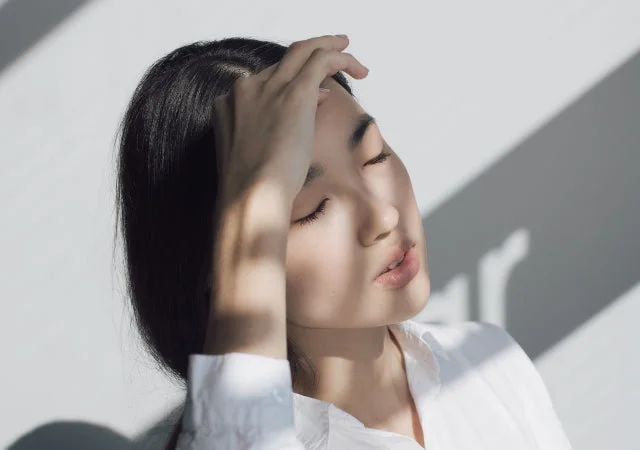 日差しの中で目を閉じ、額に手を当てている女性のポートレート