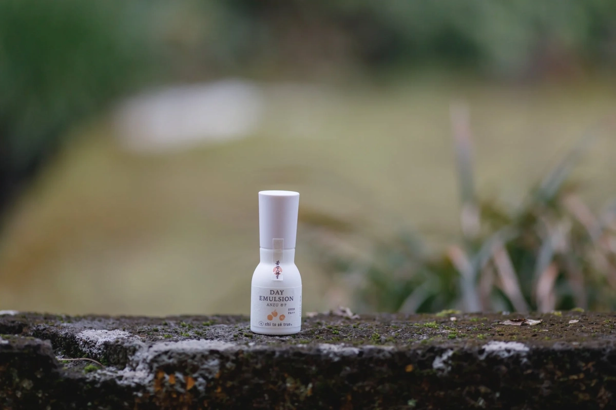 白いボトルに入った「DAY EMULSION ANZU」が、苔むした石垣の上に置かれた写真