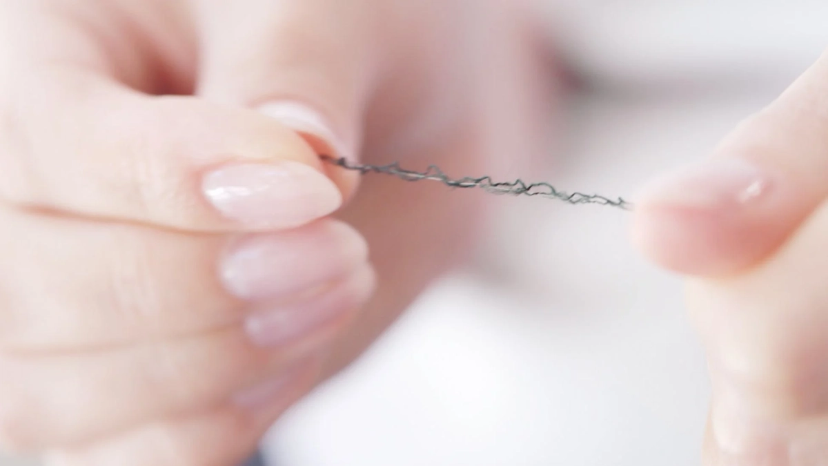 細い黒い糸をつまむ指