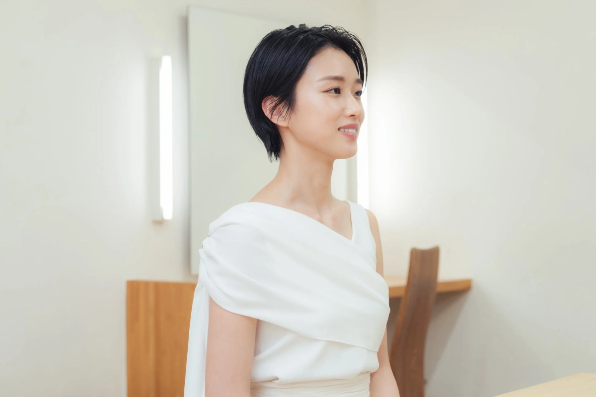 白い服を着て笑顔で右方向を見つめるショートヘアの女性