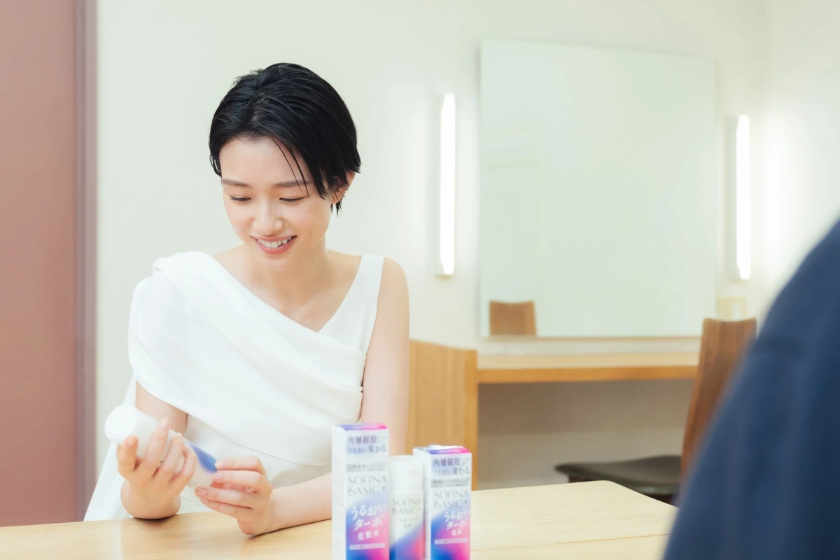 白い服を着た女性がSOFINA BASIC+の化粧品を手に笑顔
