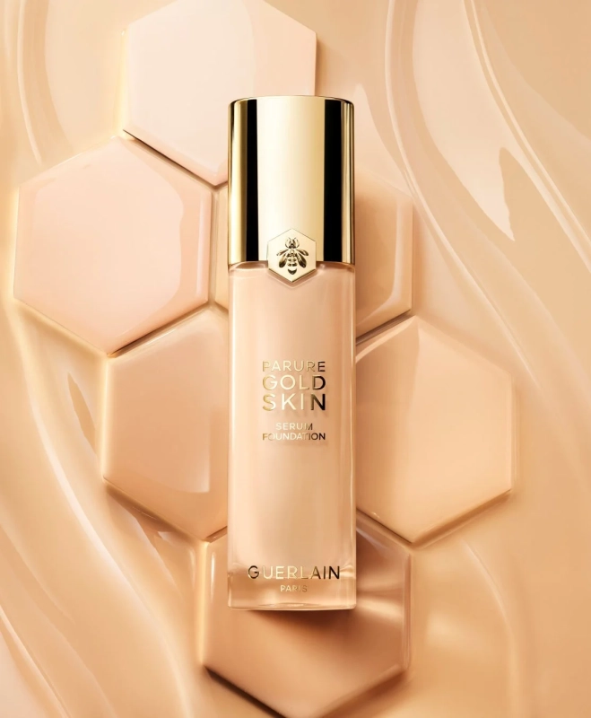 ゲランのPARURE GOLD SKIN SERUM FOUNDATIONのボトルが、ハニカム状のタイルと液体の質感を背景に配置された画像です