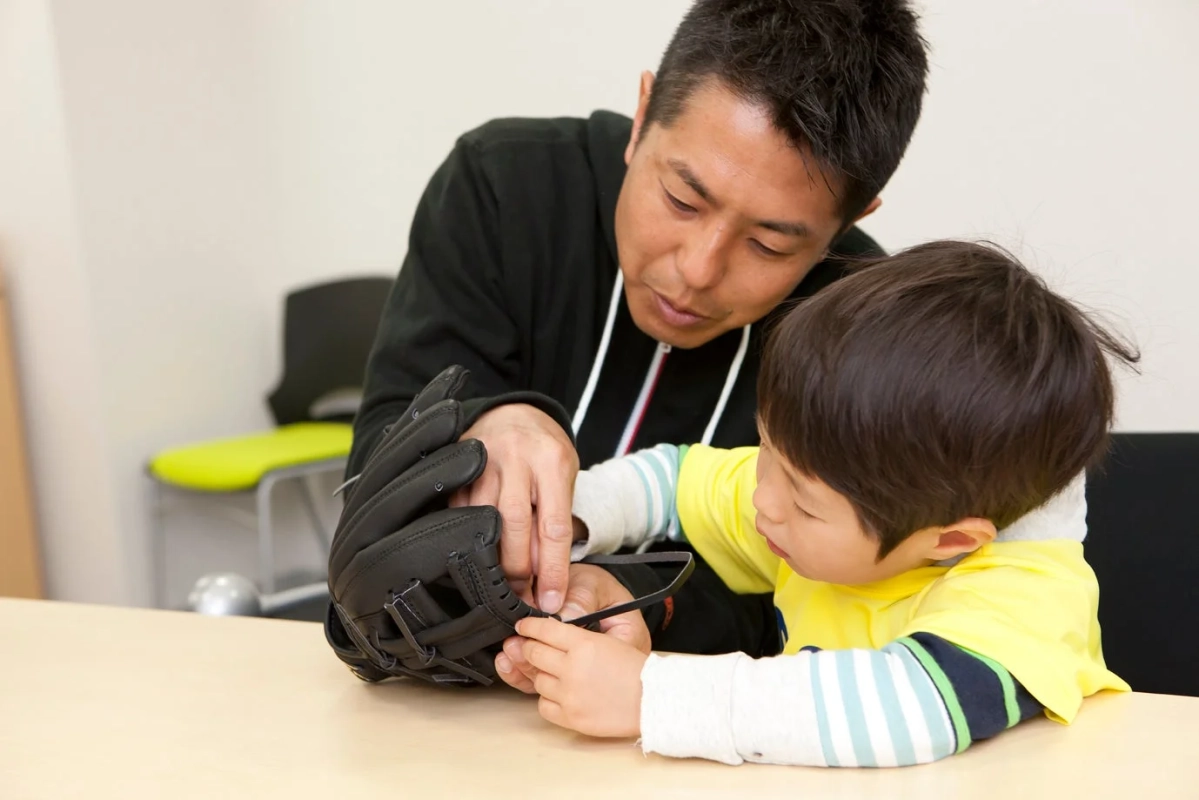男性が子供に野球のグローブの紐の扱い方を教えている様子。