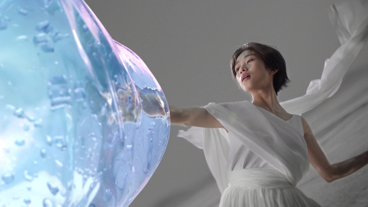 白い衣装の女性が水滴をまとった透明な物体に触れている